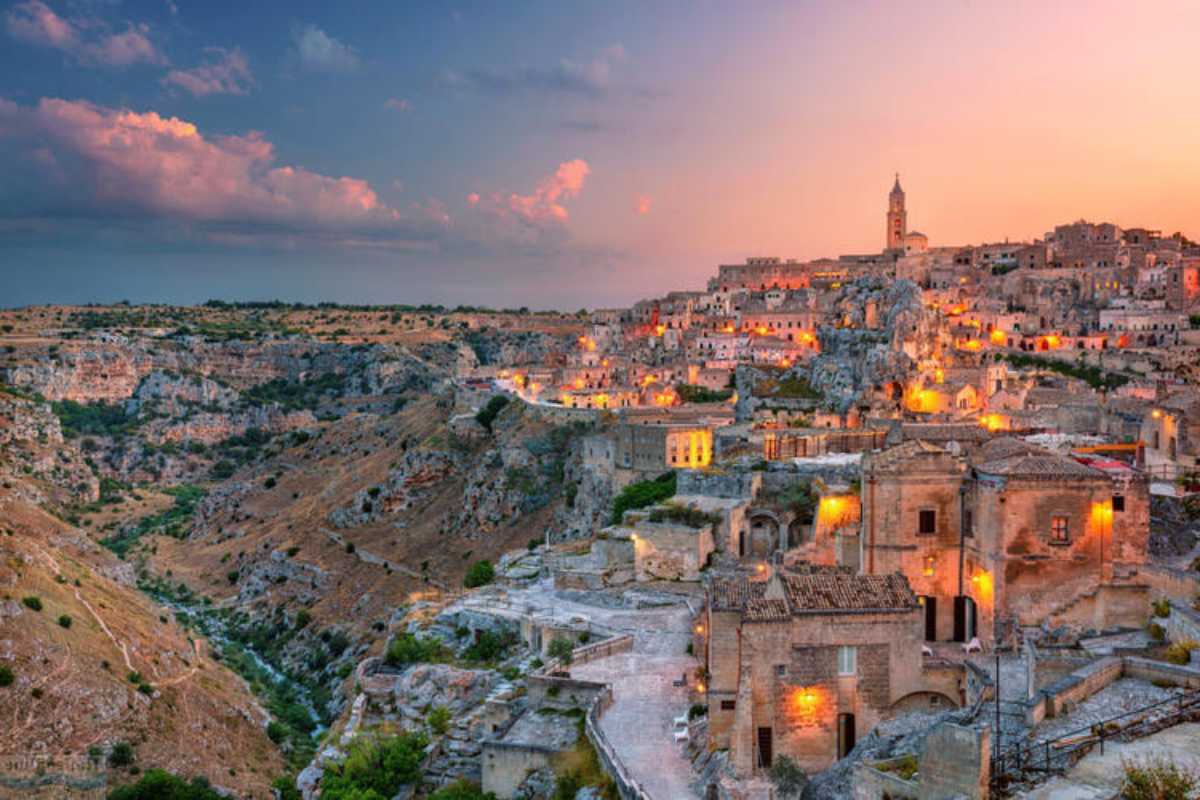 Scorcio serale di un ristorante nei Sassi con tavoli all'aperto e vista sui Sassi illuminati, atmosfera romantica