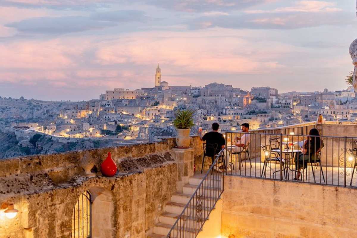 Vista panoramica al tramonto sui Sassi di Matera, con escursionisti che percorrono un sentiero nel Parco della Murgia Materana, atmosfera naturale e selvaggia